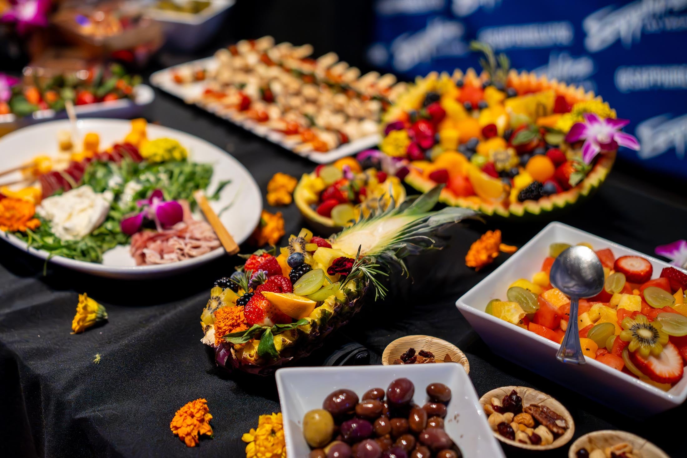 A buffet table with various dishes of food including fruits, nuts, olives, and meat.
